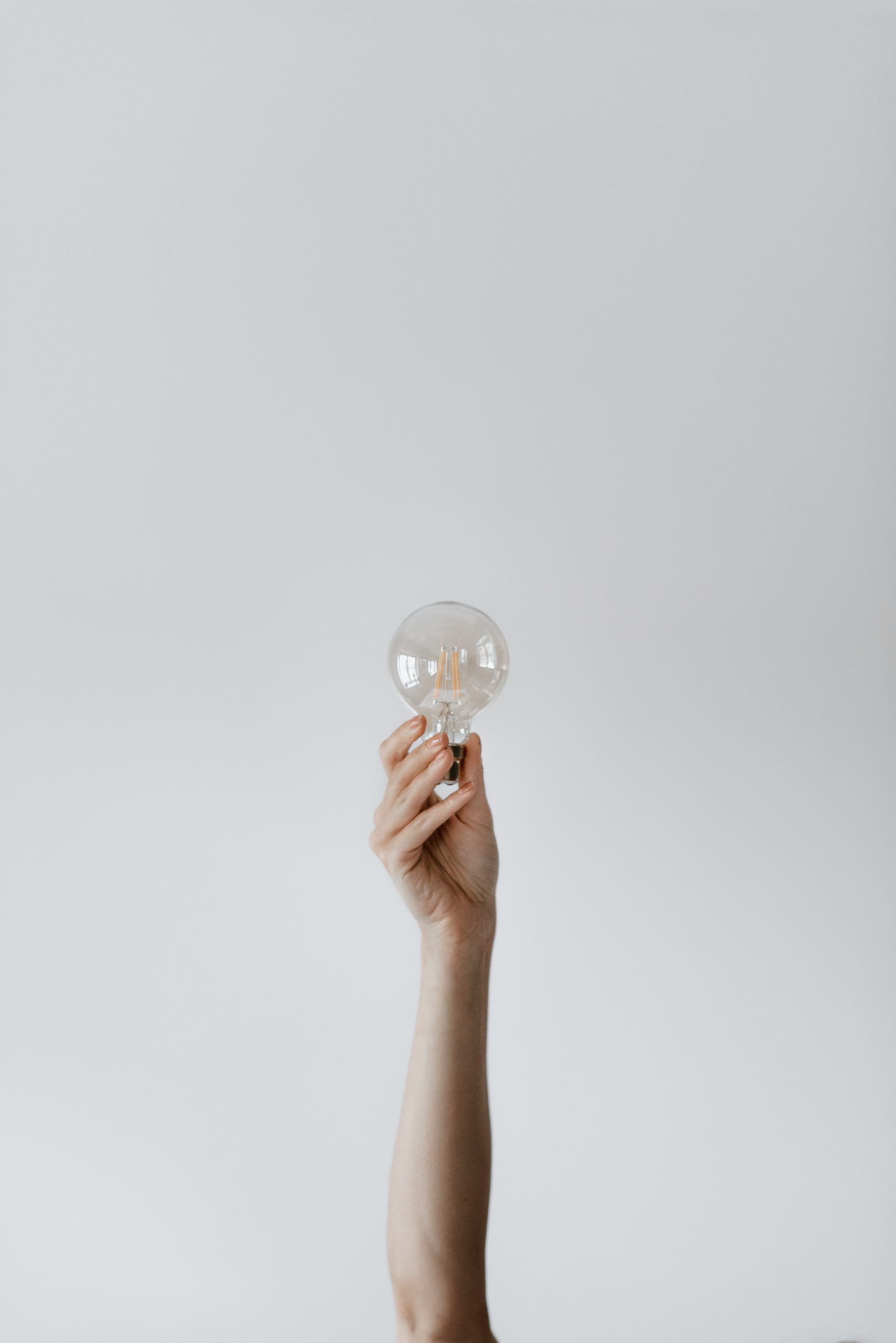 Arm reaching from the bottom of the image extends straight and holds the base of a lightbulb mid-image